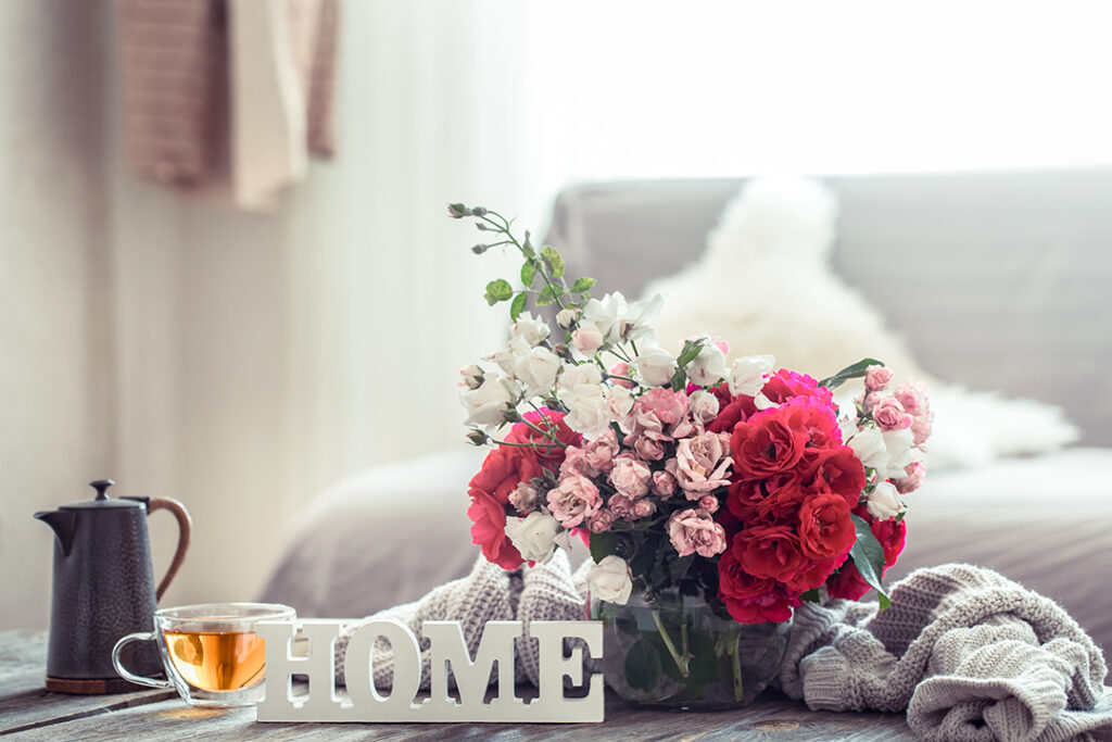 Still-life with an inscription house and a vase with flowers of different roses. The concept of home comfort and decor.
