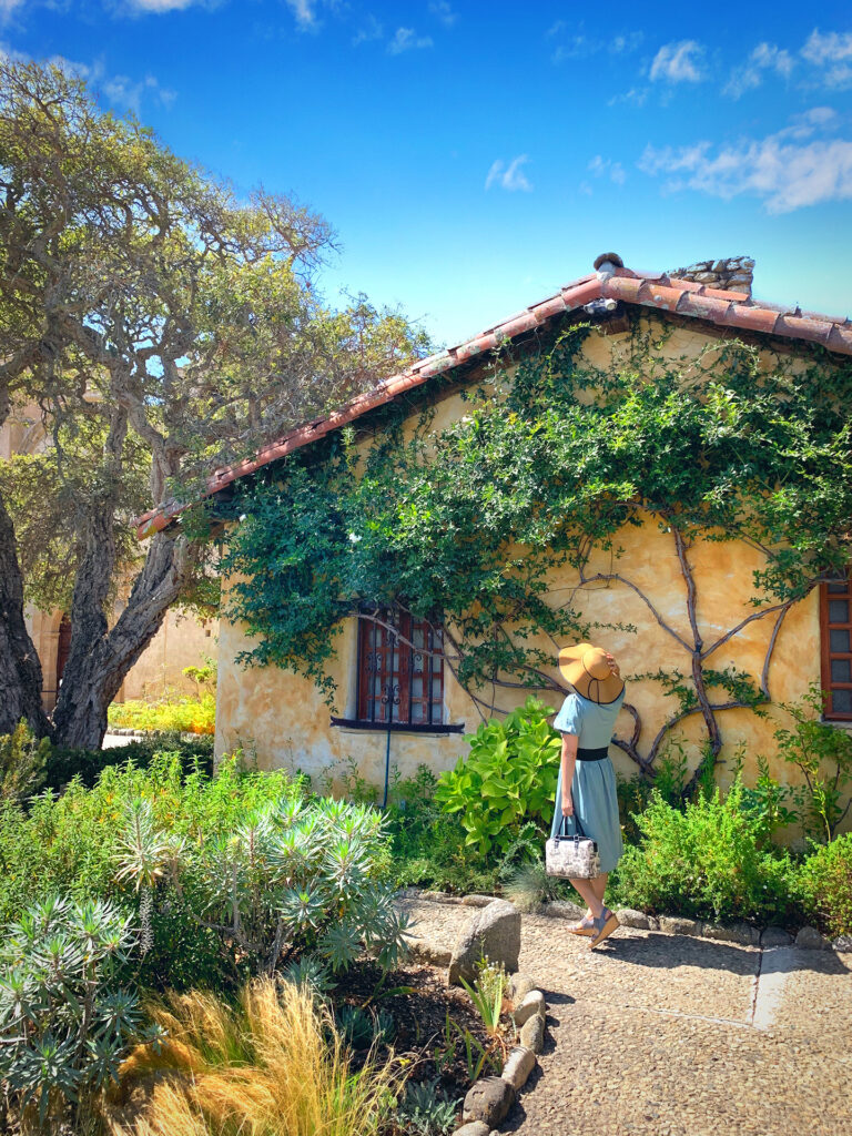 Rustic cottage on a sunny day in the garden of the Carmel Basilica Mission in Carmel by the Sea, California.  Girl wearing straw hat with white handbag.