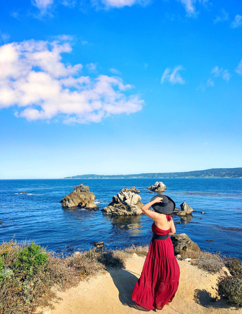 Girl in black hat and long red dress enjoying the ocean view at Point Lobos State Park, Whaler's Cove.