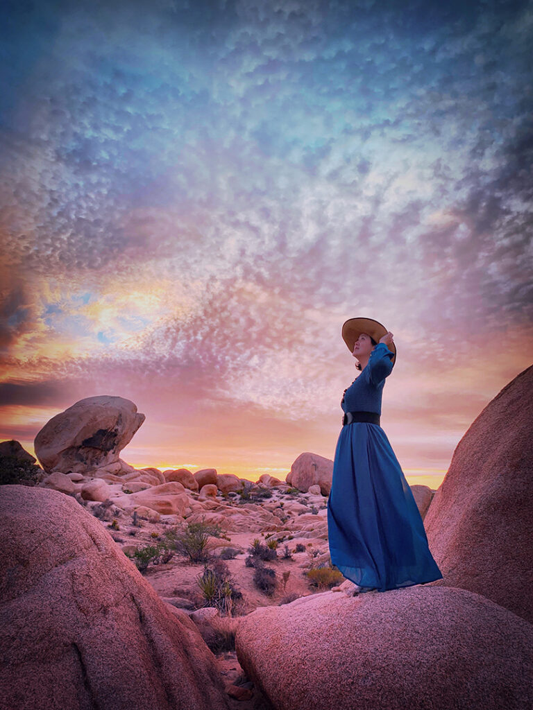 Girl in long blue maxi dress and straw hat at sunset in Joshua Tree National Park
