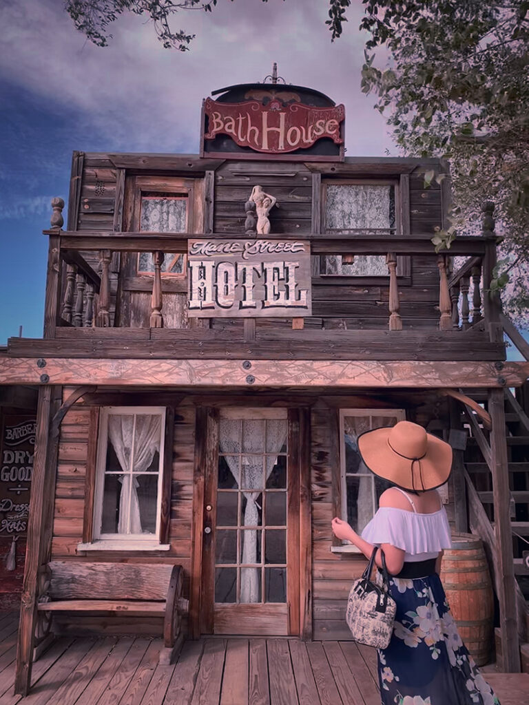 Girl in white and blue flower maxi dress and straw hat with purse standing front of old west hotel in Pioneertown Joshua Tree